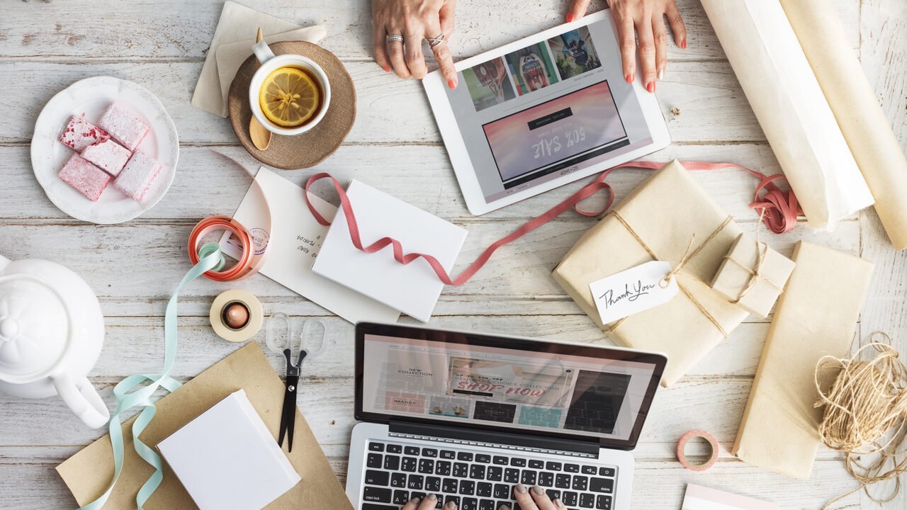 Styled overhead shopping workspace with laptop, tablet, and wrapped orders